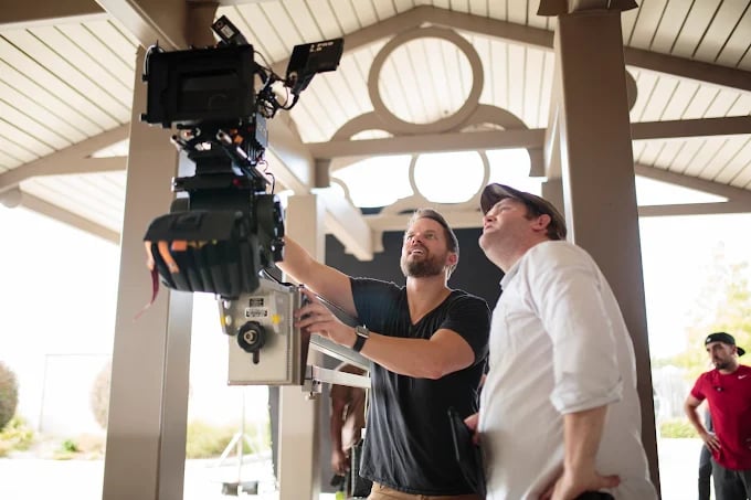 Film crew adjusting camera equipment under architectural structure